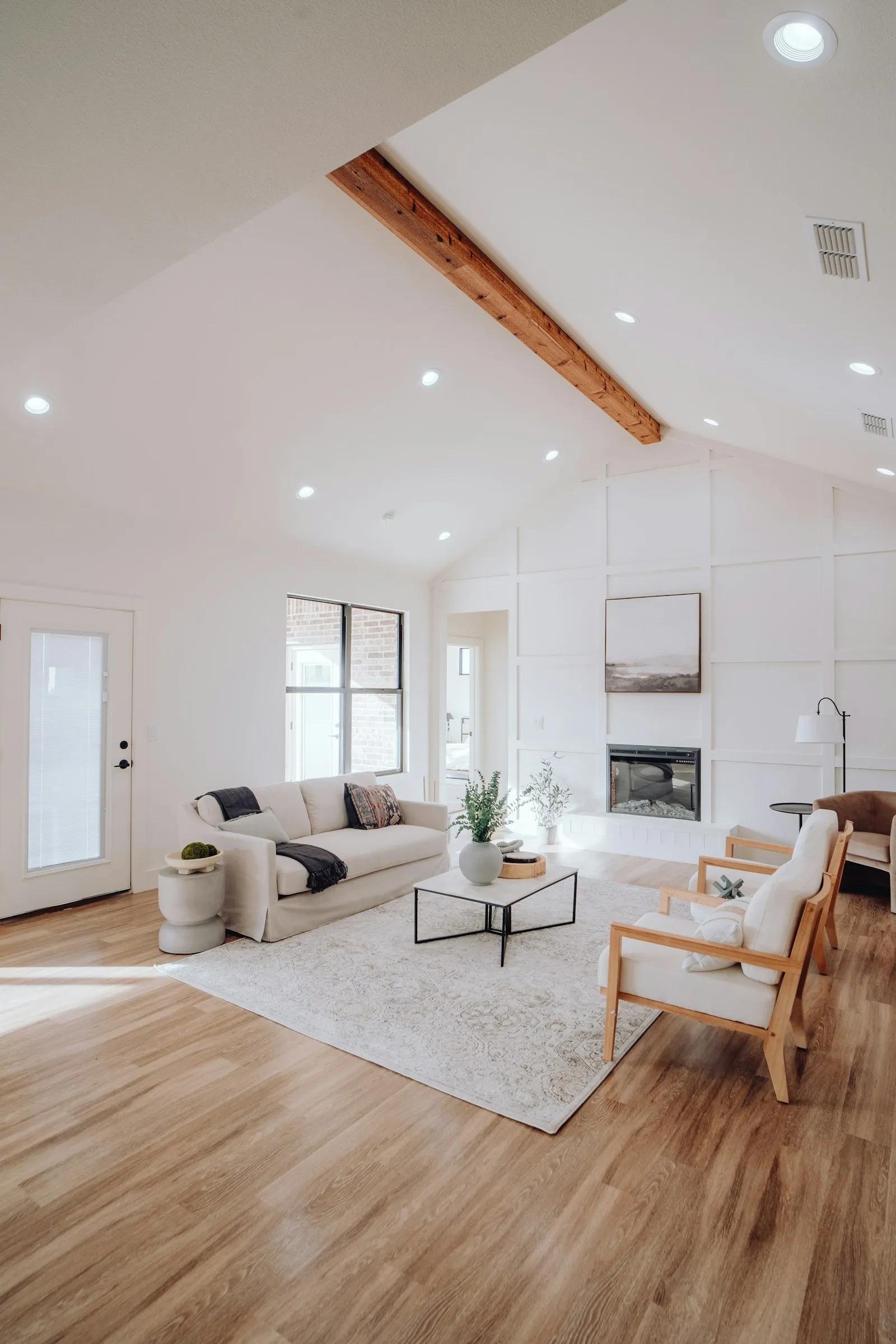 A bright staged living room with a cream sofa, timber armchairs and a pale rug on a wooden floor